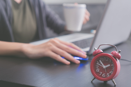 Close up of red clock on the desk, Afternoon time, Casual young woman using a laptopの写真素材