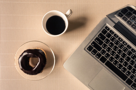 Top view of laptop with coffee cup and donut on table.の写真素材