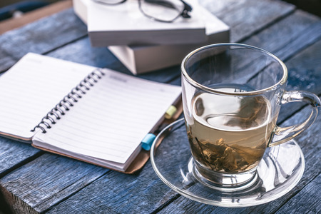 Cup of tea with notebook and glasses on wooden tableの写真素材