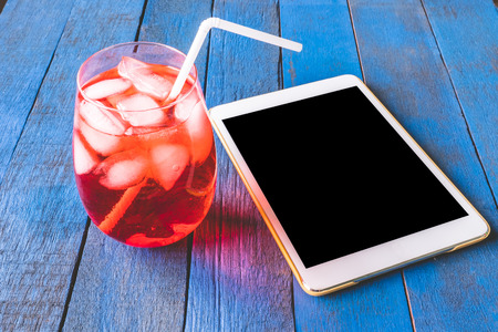 Tablet and red cocktail on blue painted wood plank background.の写真素材
