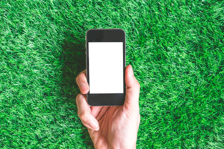 Male hand holding smart phone on green grass background.の写真素材
