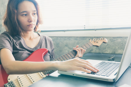 Young woman playing guitar and using laptop on the table at home.の写真素材