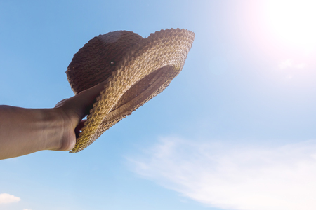 Male hand holding hat in front of sun, blue sky on backgroundの写真素材