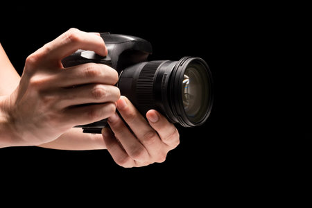 Male hand holding a digital camera on a black background.