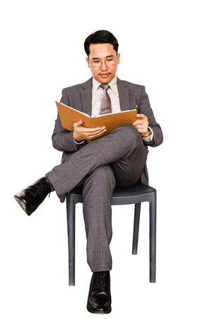 Businessman is sitting on a chair and reading a book, isolated on white background.の写真素材