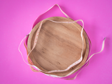 Empty wooden dish with tape measure on pink background.の写真素材