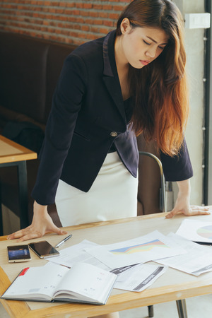 Asian businesswoman working at office desk, looking tired.の写真素材