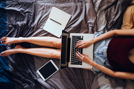 Close up of young woman using laptop while sitting on her bed,  Films grain filter.の写真素材