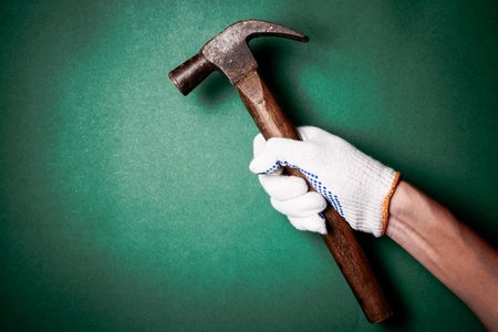 Hammer in hand with protection glove on green background. Free space for textの写真素材