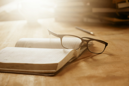 Close up of open notebook with eyeglasses on wooden desk, Soft focus,  Flare sun light,Vintage tone.の写真素材