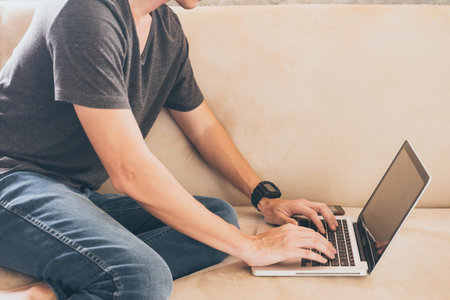 Close up of casual young man sitting on sofa and using a laptop at home.