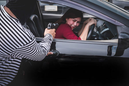 Robber pointing a gun to scare young woman and try to rob her car.の写真素材