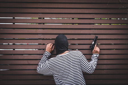 Robber hiding behind the wall, looking at victims and waiting to come nearest for stealing the...