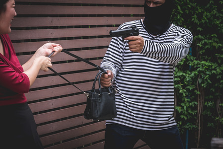Thief threatening with gun, young woman fight over with robber who stealing bag.の写真素材