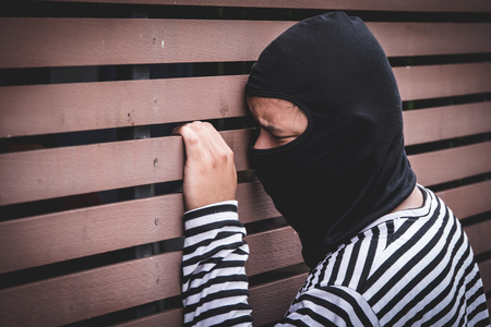 Robber hiding behind the wall, looking at victims and waiting to come nearest for stealing the valuables.の写真素材