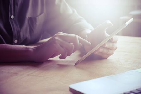 Close up of Male hands using tablet on the table, toned with sunlightの写真素材