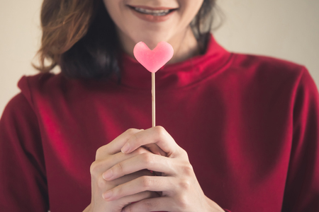 Portrait of Happy asian woman dressed in red sweater holding pink heart candy.の写真素材