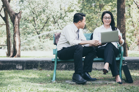 Happy Asian business people are dicussing, working and relaxing while sitting in the park.の写真素材