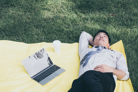 Asian businessman is sleeping on a lawn in a park after finish work.の写真素材