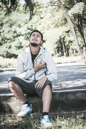 An Asian young man has a heart pain while exercising in a park.の写真素材