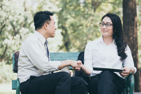 Happy Asian business people are dicussing, working and relaxing while sitting in the park.の写真素材