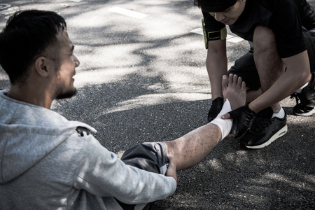 A man uses elastic bandage for pain relief one man's ankle after a workout in a park.の写真素材