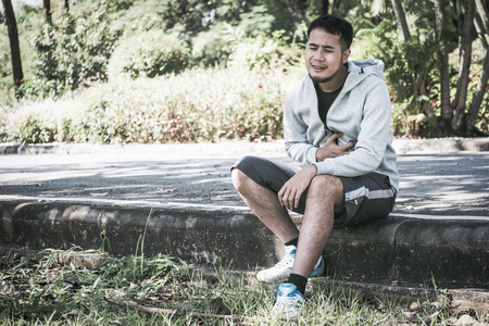 An Asian young man has a chest pain while exercising in a park.の写真素材