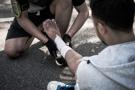 A man uses elastic bandage for pain relief one man's ankle after a workout in a park.