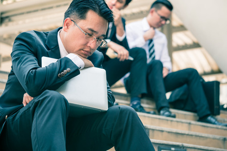 Asian Businessman tiring and sleeping on his laptop while sitting on stairs in the city.の写真素材