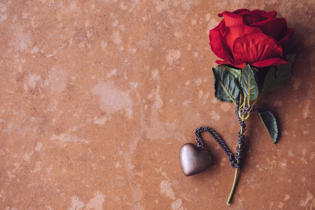 Red rose with silver heart necklace on brown grunge board background. Free space for text. Concept of Valentine Day.の写真素材