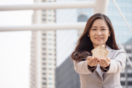 Attractive business woman holding house model with urban scene background. Real estate conceptの写真素材