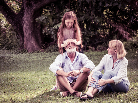 Happy family having fun together in the garden. Father, mother and daughter sitting on grass in a park.の写真素材