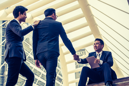 Asian businessman is shaking hands with his new partner while sitting on stairs in front of the office building. Vintage toneの写真素材