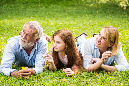 Happy family having fun together in the garden. Father, mother and daughter laying down on grass in a park.の写真素材