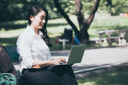 Asian business woman working on laptop while sitting on the bench in the park.の写真素材