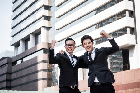 Portrait of two young Asian businessmen in black suit standing with office building backgroundの写真素材