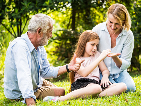 Happy family having fun together in the garden. Father, mother and daughter sitting on grass in a park.の写真素材