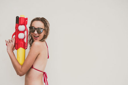 Attractive young woman in the red bikini holding water gun on white background