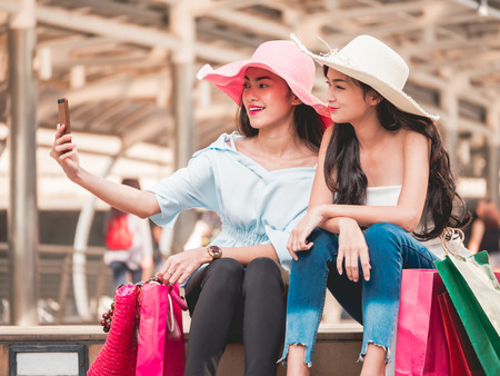 Two beautiful young women sitting on the stairs and making self-portrait by smart phone after enjoying in shoppingの写真素材