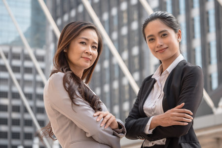 Two Asian business women smiling with urban scene background. Teamwork and success concept