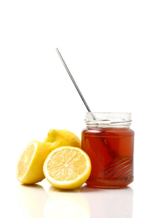 A glass of honey with dipper and lemon on a white backgroundの写真素材