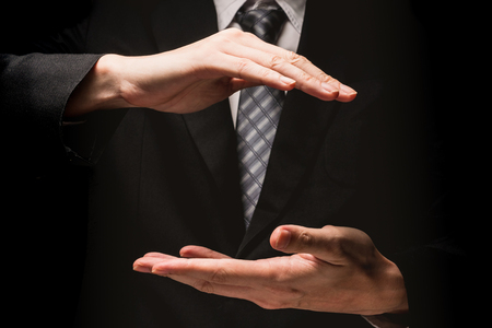 Close up of man in black suit with hand gesture on black background.の写真素材
