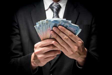 Close up of man in black suit holding a lot of cash on black backgroundの写真素材