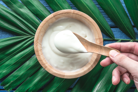 Top view of yogurt in wooden bowl on green leaves backgroundの写真素材