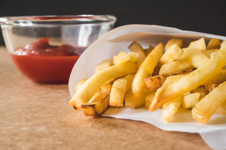 Close up of French fries with ketchup on wooden table.の写真素材