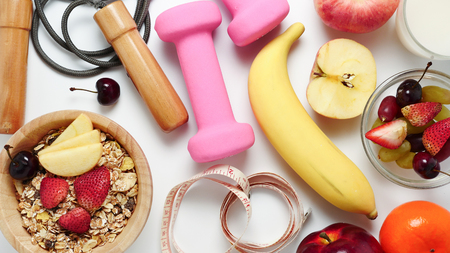 Top view of Oatmeal flakes, milk, fresh fruits and fitness equipments on white background.の写真素材
