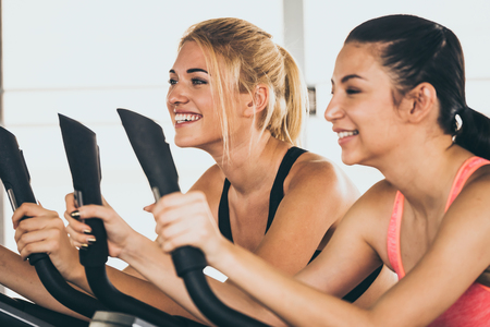 Attractive young women working out together on exercise bike at the gym.の写真素材