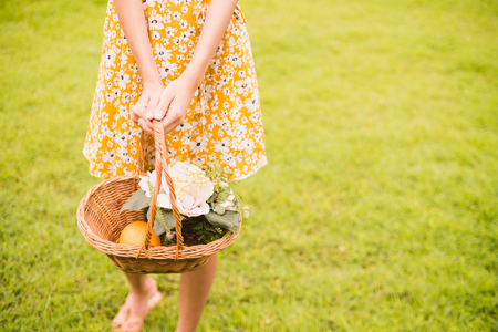 Close up of woman in yellow dress holding a basket with flowers standing on green grassの写真素材