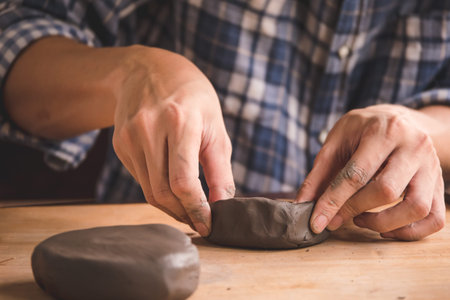 Male hands modelling a block of clay on wooden table