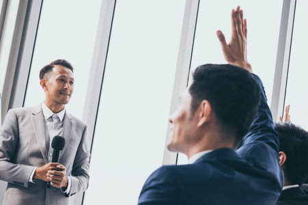 Audience raising hands up while businessman is speaking in training at the office.